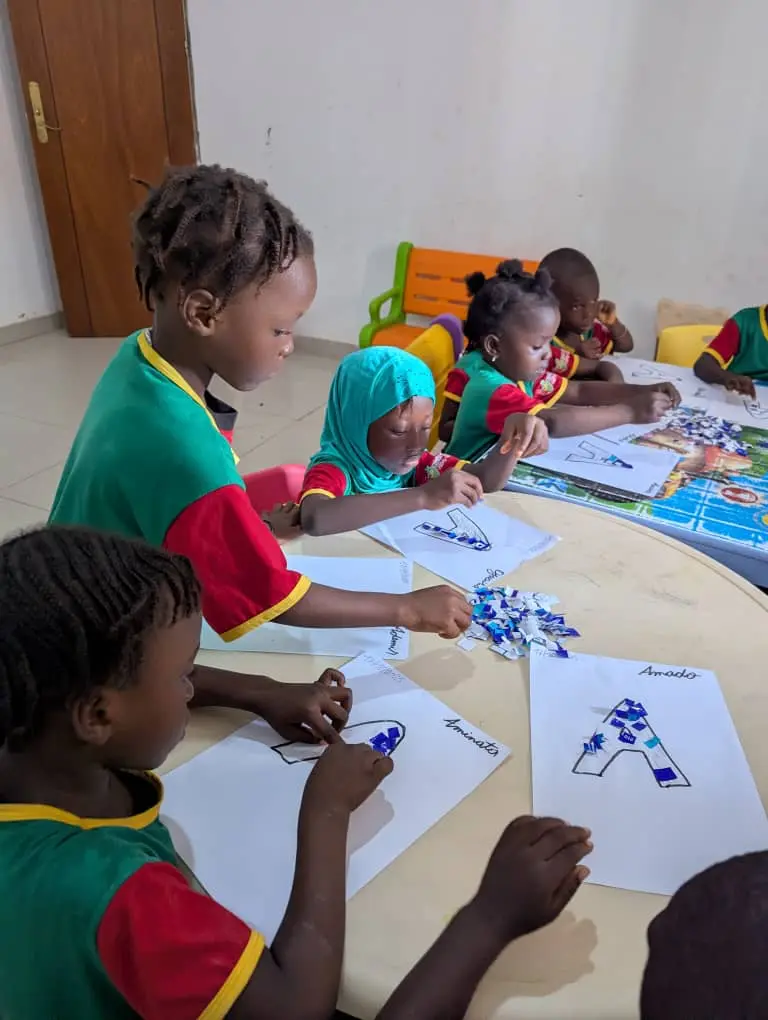 Crianças colando recortes de papel colorido sobre desenhos da letra A