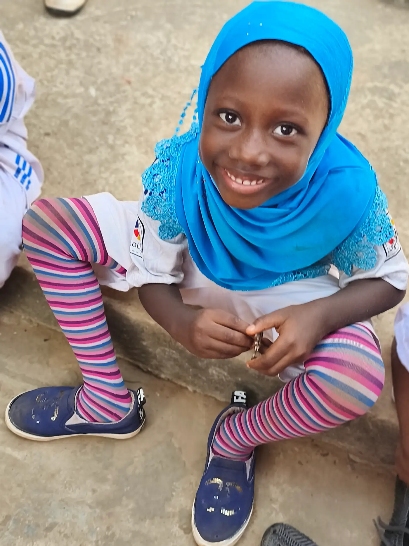 Menina de hijab azul agachada e sorrindo para a câmera