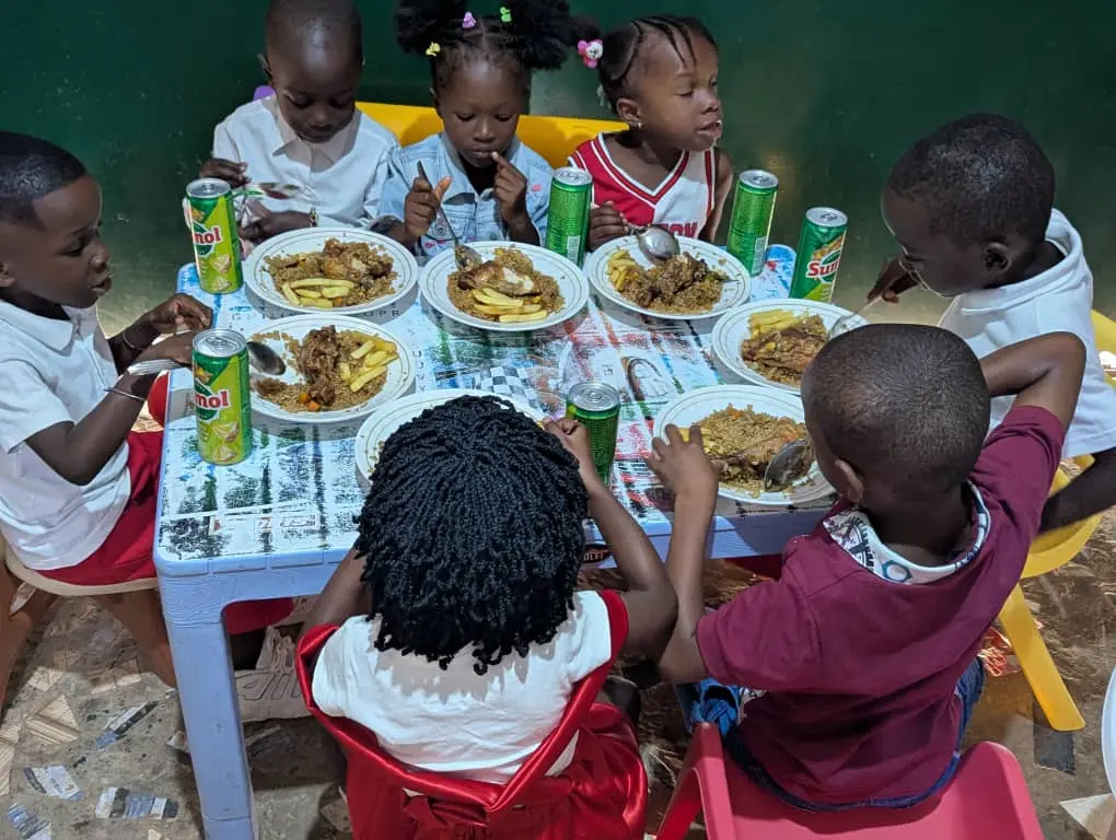 Crianças sentadas à mesa redonda comendo arroz com frango, latas de refrigerante Sumol sobre a mesa