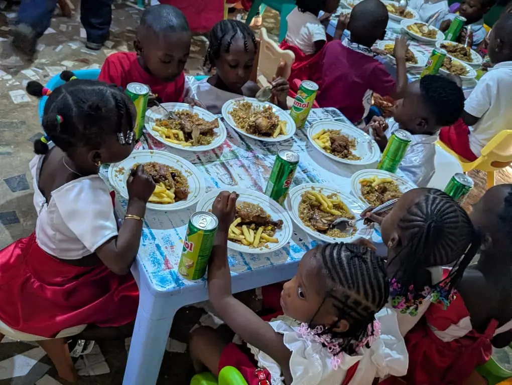 Grupo de crianças ao redor de mesa redonda com pratos de arroz e latas de refrigerante