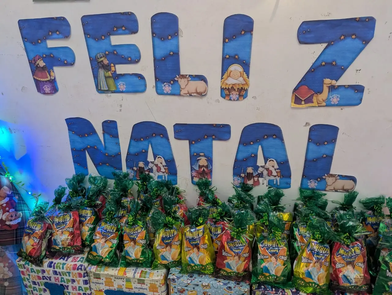 Decoração de Natal na parede com a frase Feliz Natal e lembrancinhas de salgadinho embaixo
