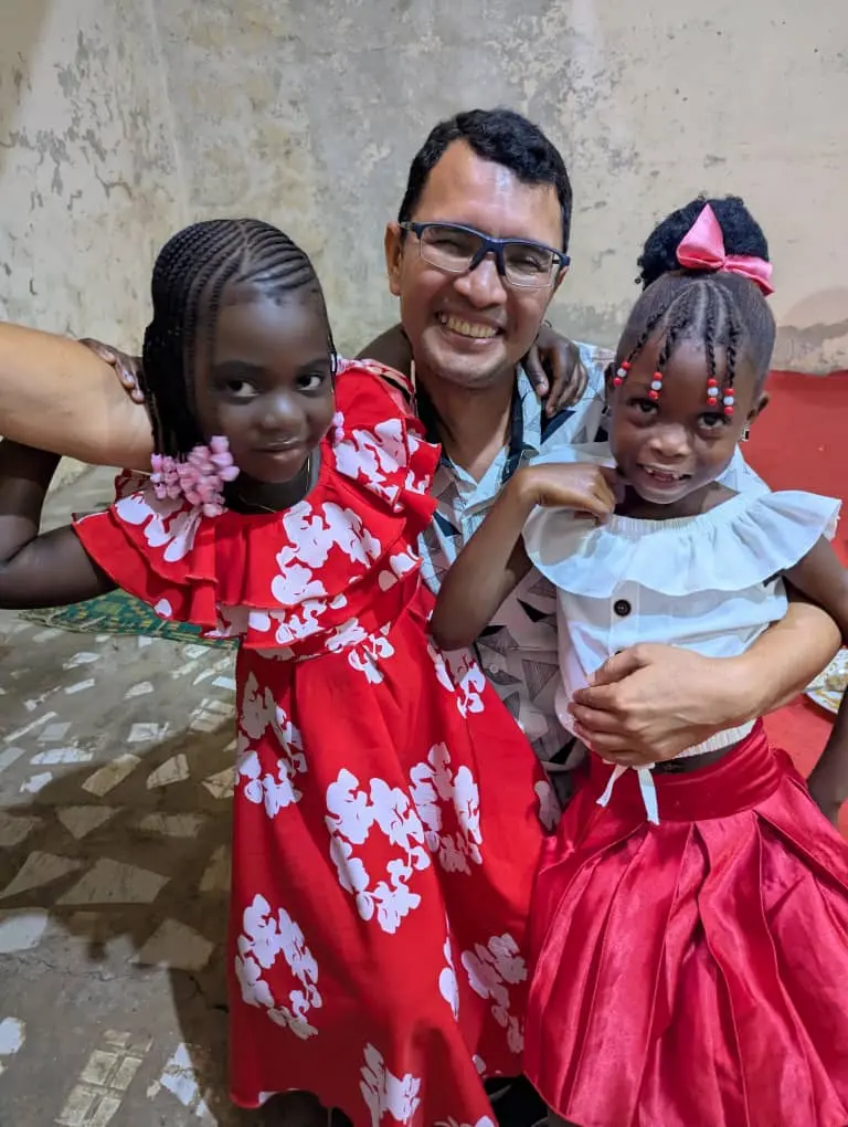 Homem posando com duas meninas vestidas para uma festa, uma de vermelho e outra de branco